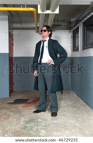 Police lieutenant in an achetypal outfit, with suit and long over coat in a basement, posing in front of a crime scene