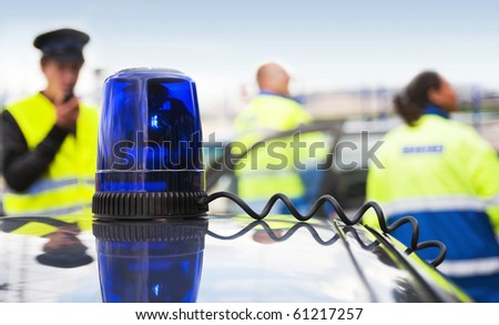 Blue flashlight on top of an unmarked police car, with a team of emergency medical service personnel in the background