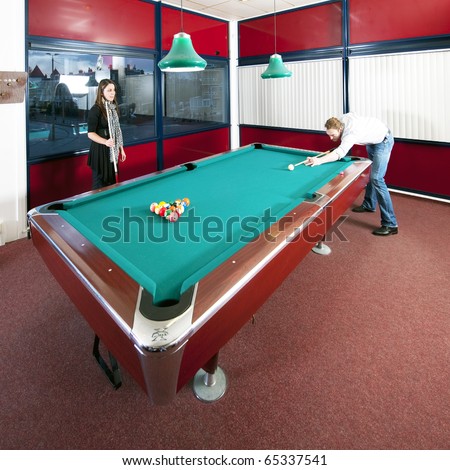 Two people playing pool in a room with a view on an city skyline at dusk