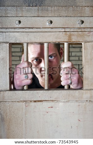 Prisoner with a split lip holding the bars of his jail cell door
