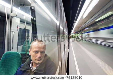 Man, sitting in a metro at night, passing a station, looking out the window with a weary  and tired look in his eyes