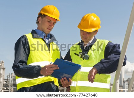 Two petrochemical engineers wearing safety vests and a hard top going over a checklist