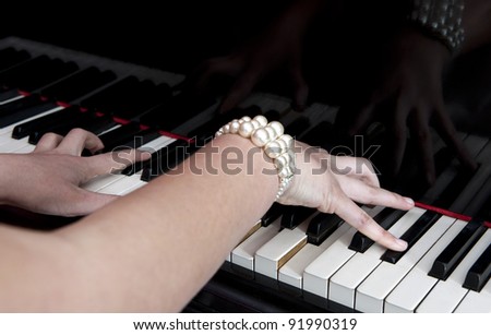 Two female hands playing a grand piano, focus on the woman\'s right hand fingers.