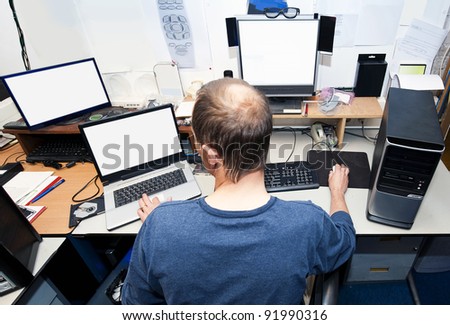 Man behind a desk with several computers and screens, repairing and installing new hardware