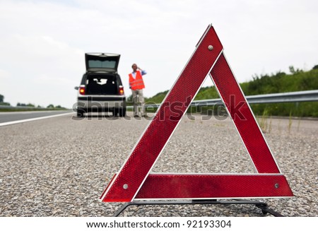 Road side warning triangle, warning oncoming traffic of a broken down car, with a man using his cell phone to call for assistance