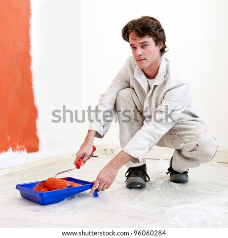 Painter, kneeling down to refill his paint roller with orange paint, whilst redecorating a room