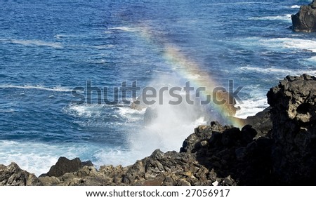 ocean surf waves break on the rocky coast and real rainbow in sunny summer day