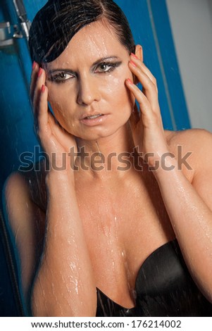 Beautiful wet brunette woman in sexy black lingerie standing dripping water with her hands raised to her head and a serious expression looking to the right side of the frame, high angle view
