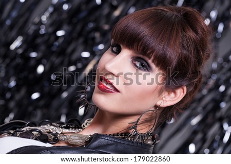 Beautiful glamorous sexy woman with her brunette hair cut in a fringe wearing trendy jewellery looking at the camera with parted red lips against a bokeh background