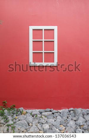 white window on red wall with rock at the bottom