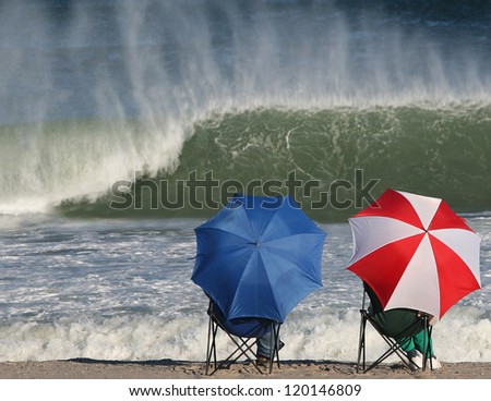 Large wave about to break as people on beach sit beneath beach umbrellas