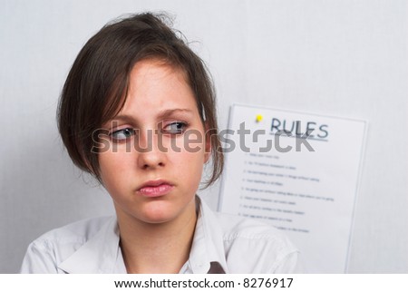 Teenage schoolgirl looks unhappy as she ponders a list of rules.