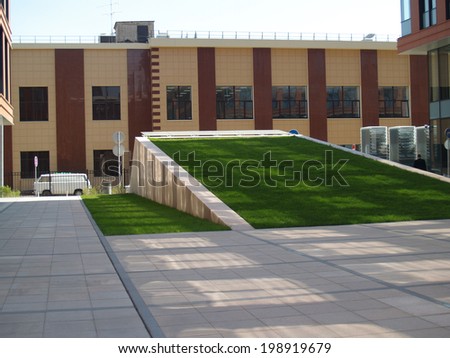 Grass slide in  inner yard of a city building with square spots of lights and shades