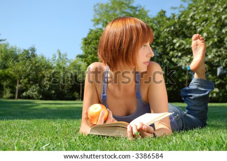 Girl lying in a meadow with apple and book