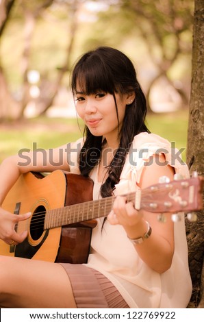 asian girl playing guitar under a tree in the garden