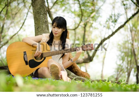 asian girl playing guitar under a tree in the garden