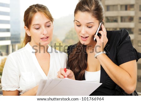 Two beautiful young executives reading some papers and one of them is on the phone