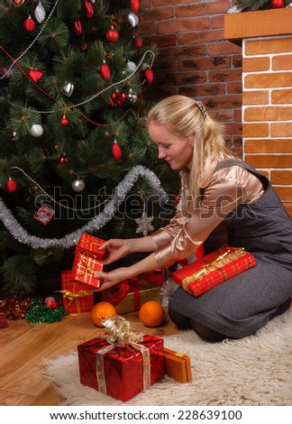 Young beautiful woman in a business attire putting gift boxes under the Christmas tree