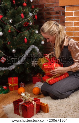 Young blonde woman in a business attire putting the presents under the Christmas tree