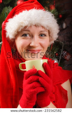 Close up of smiling woman in Santa hat and red scarf sitting with mug of hot drink in her hands