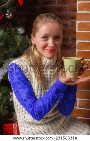 Beautiful woman in blue lace blouse and white knitted tunic with green cup in her hands