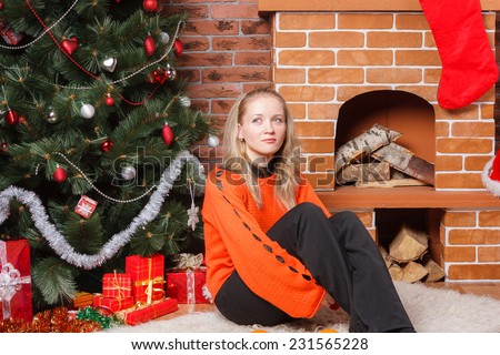 Beautiful blonde haired girl sitting next to decorated Christmas tree and thinking