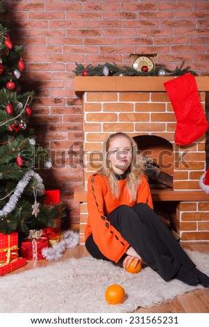 Beautiful blonde haired woman sitting next to decorated Christmas tree and fireplace