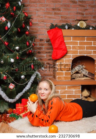Young woman in orange sweater laying nearby Christmas tree on bear rug