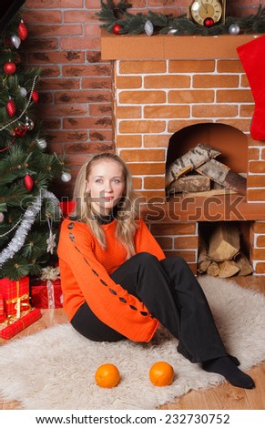 Young blonde haired woman sitting next to decorated Christmas tree and thinking