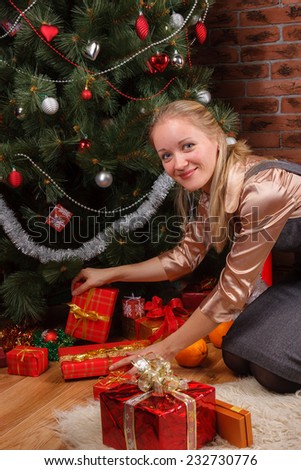 Beautiful blonde woman in business attire sorting through the gifts under the Christmas tree