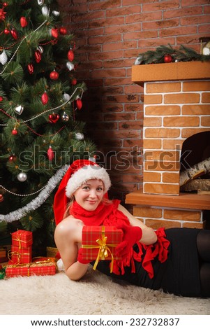 Pretty woman in Santa hat and red scarf laying under the Christmas tree with red gift box