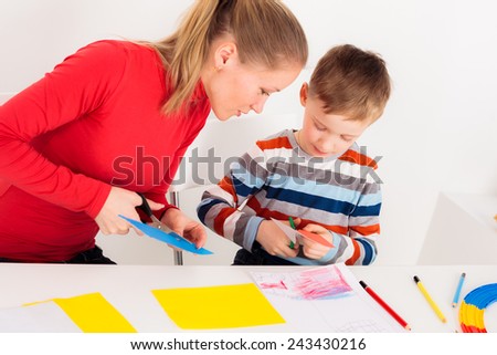Mother helping her child to cut colored paper