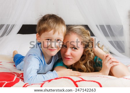 Happy woman with her child laying on belly on bed