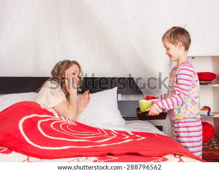 Little son giving a tray with breakfast to his mom laying in bed