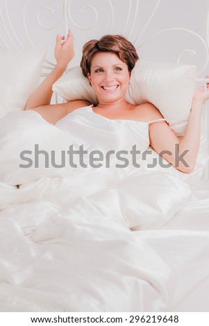 Smiling woman laying in bed on white silk sheet