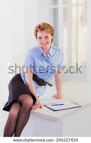 Lovely woman in nice suit sitting on white desk in  office