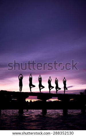 Group of silhouette yoga practicing at sunset on the bridge.
