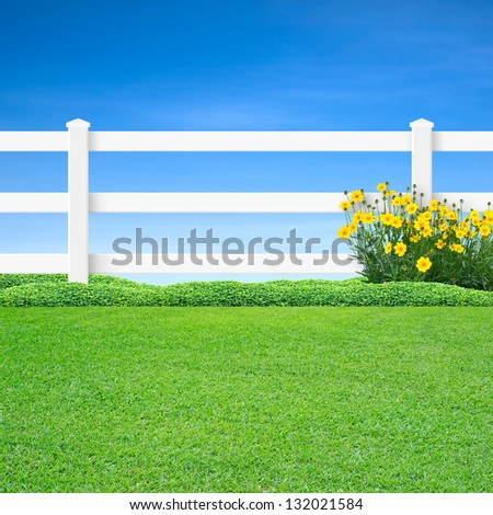 Long white fence with yellow flowers and green grass on blue sky