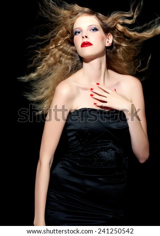 Model with blond hair wearing black silk cocktail dress on black background.