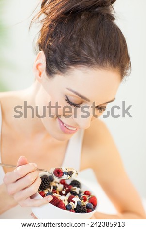 Woman eating fresh made muesli breakfast dish with oats, fresh berries. Smiling healthy eating European girl.