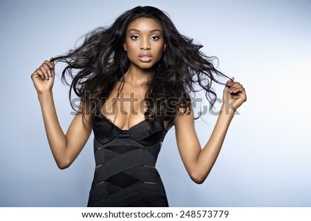 African young woman with long hair wearing small bandage black dress on blue background.