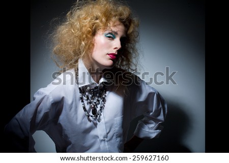 Model with fluffy hair wearing white shirt and jewelry.