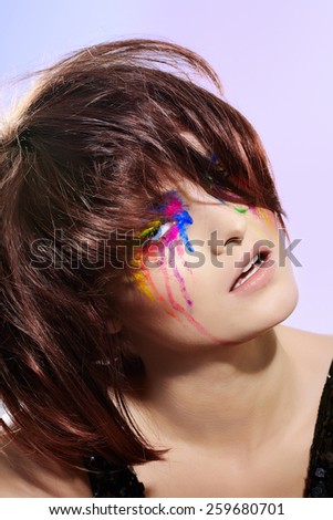Fashion model with short dark fluffy hair and colorful make-up with paint effect.