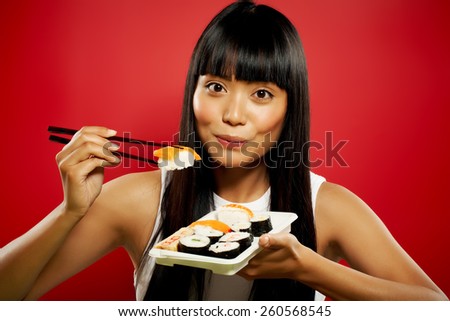 Young Asian woman eating sushi on red background.