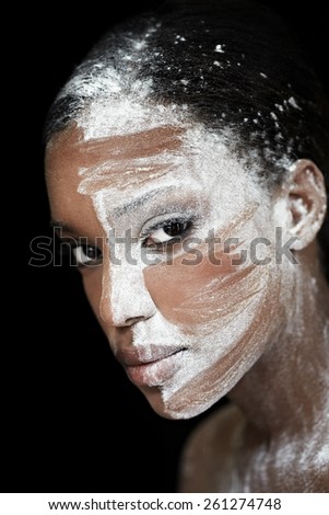Dark woman with white substance over her face. Slightly tribal look otherwise meant as artistic makeup.