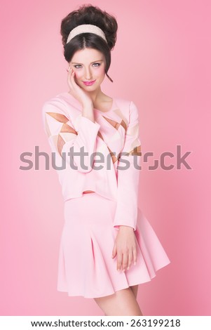 Sixties fashion woman in soft pink outfit with retro hairstyle and makeup posing over pink background.