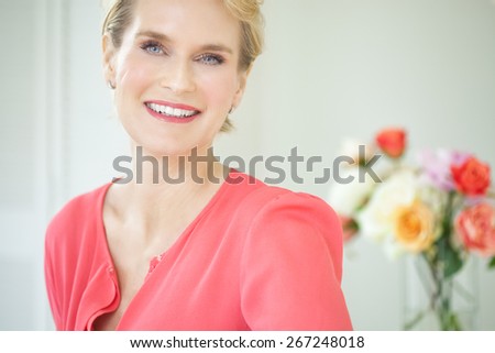 Beautiful smiling elegant woman indoors wearing pink blouse and short blond hair.