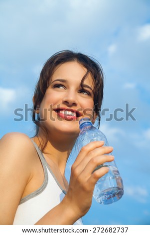 Young happy woman outdoor against blue sky with bottle of mineral water.