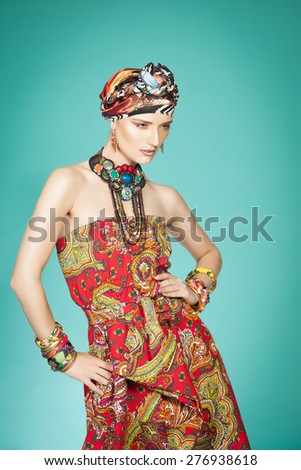 Colorful exotic gypsy style fashion woman wearing red dress and turban over cyan background.