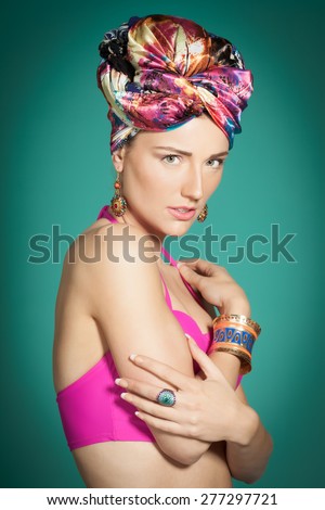 Fashion model wearing colorful style with bright pink top and turban over cyan background.